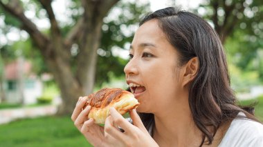 Holding ve yeşil renkli Park'ta taze pişmiş ekmek ekmek yeme Asyalı kadın