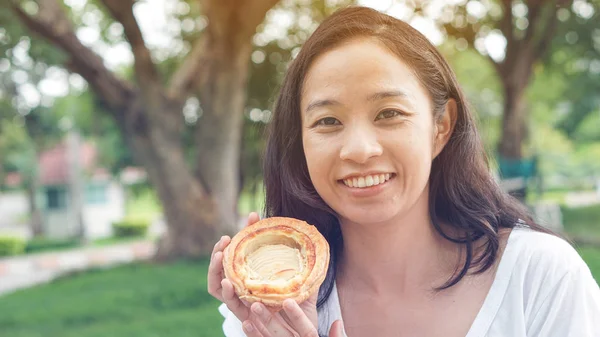 Aziatische vrouw houden en eten vers gebakken bakkerij in groene backg — Stockfoto