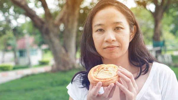 Asian woman holding and eating fresh baked bakery in green backg — Stock Photo, Image