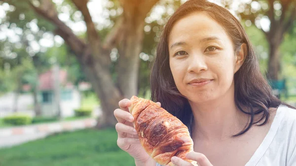 Aziatische vrouw houden en eten vers gebakken bakkerij in groene backg — Stockfoto