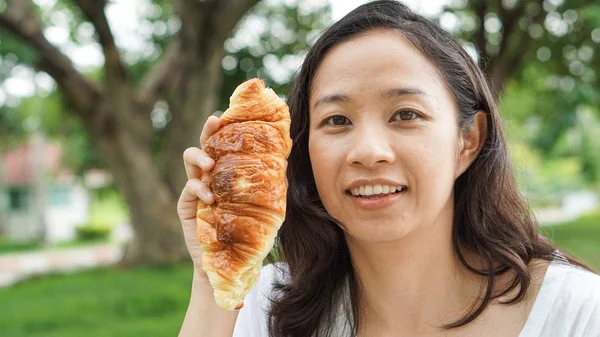 Aziatische vrouw houden en eten vers gebakken bakkerij in groene backg — Stockfoto
