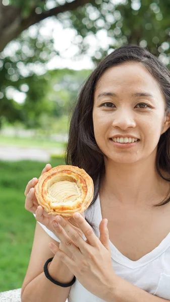 Aziatische vrouw houden en eten vers gebakken bakkerij in groene backg — Stockfoto