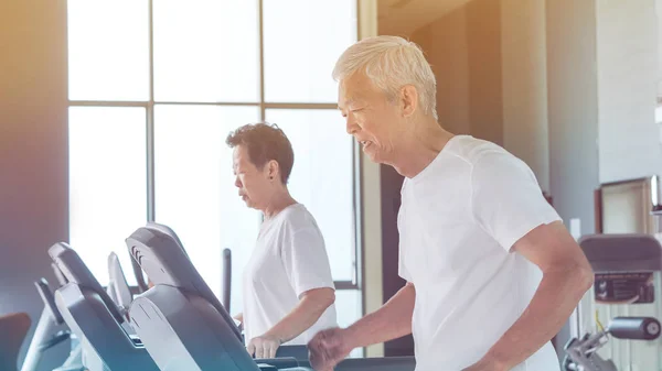 Healthy Asian senior couple exercise together in gym running tre