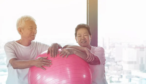 Happy senior Asian couple have fun with gym yoga ball class