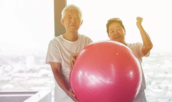 Happy senior Asian couple have fun with gym yoga ball class