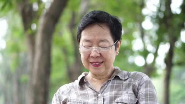 Asiatisk senior kvinna sitter och läser en bok i gröna naturparken bakgrund — Stockvideo