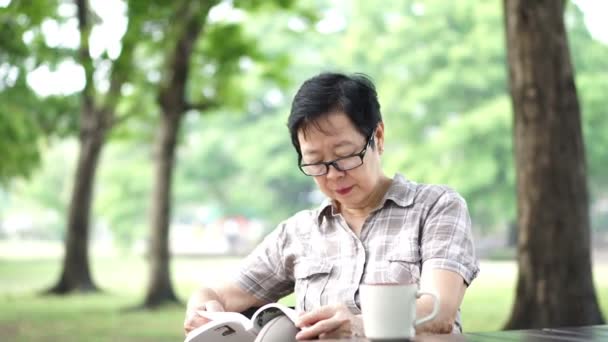 坐在亚洲高级女人和书中的绿色自然背景公园 — 图库视频影像