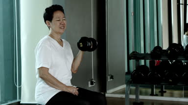Asyalı kadın kıdemli kaldırma dambıl, sağlıklı fitness salonunda egzersiz