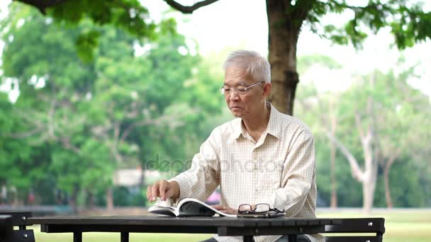 Asiatiska senior man läser boken ensam i parken — Stockvideo