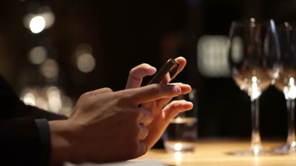 Hand mit Smartphone im Luxusrestaurant mit Weingläsern — Stockvideo