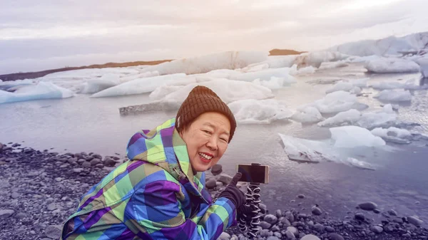 Asian old woman happy taking photo with smartphone glacier lagoo — Stock Photo, Image