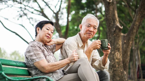Asian senior couple relax drinking coffee in summer park, green — Stock Photo, Image