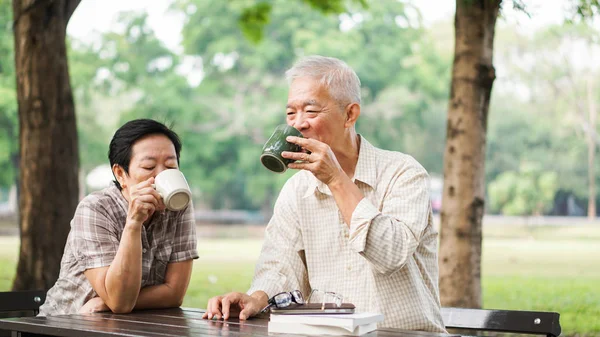 アジアのシニア カップル リラックス グリーン夏の公園でコーヒーを飲む — ストック写真