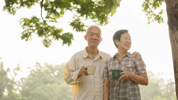Азиатская старшая пара расслабиться пить кофе в летнем парке, зеленый — стоковое фото