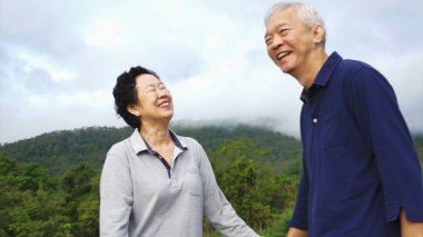 Doğada dağ yürüyüşü yaparken Asyalı yaşlı çift gülüyor