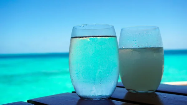 Clear glass water cocktail with blue turquoise ocean background — Stock Photo, Image