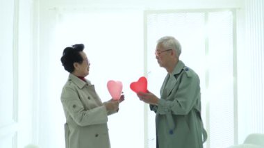 Asyalı yaşlı çift, kırmızı kalp balonu takası yapıyor. Yıldönümü aşkı.