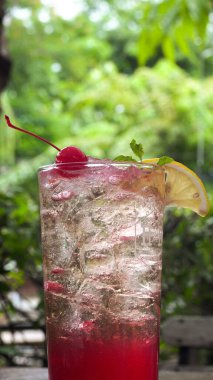 Yeşil arka planda limonlu soğuk kırmızı kiraz gazozu.