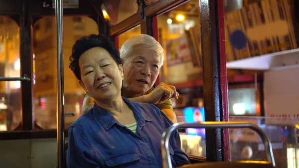 Asian elder couple have fun travel through Hong Kong city tram at night