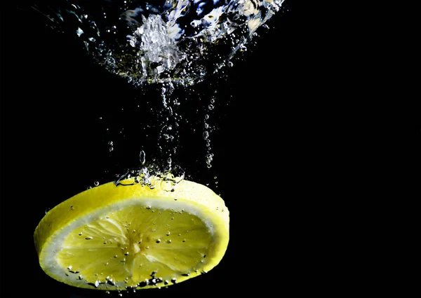 Шматочок жовтого лимона падає у воду — стокове фото