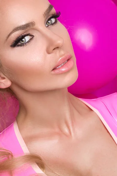 Красивая женщина модель с длинными светлыми волосами одета в розовое платье стоя на розовом фоне и радостно улыбается — стоковое фото