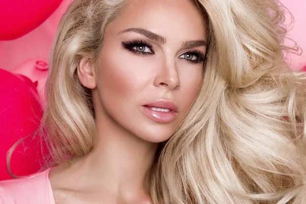 Pembe bir arka plan ve sevinçle gülümsüyor üzerinde pembe elbise duran uzun sarı saçlı güzel kadın modeli giymiş