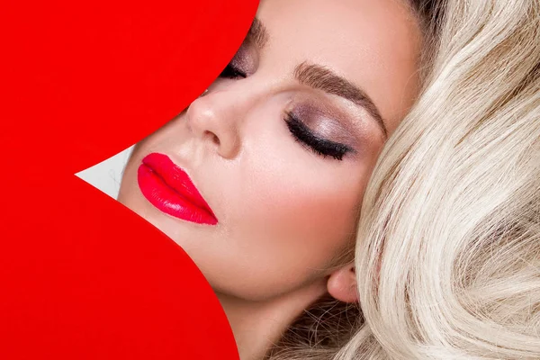 Güzel bir kadınla uzun sarı saç ayakta beyaz bir arka plan üzerinde kırmızı iç çamaşırı giymiş ve elinde kırmızı bir kalp Sevgililer günü tutar