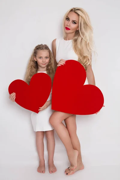 金髪の美人母と娘の白い背景の上に立って、彼の手に赤いハート — ストック写真