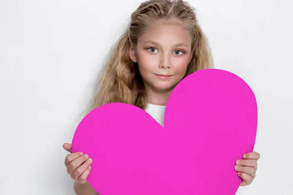 Jolie petite fille étonnante petite princesse, tenant un cœur rose dans ses mains et debout sur un fond blanc dans la robe blanche — Photo