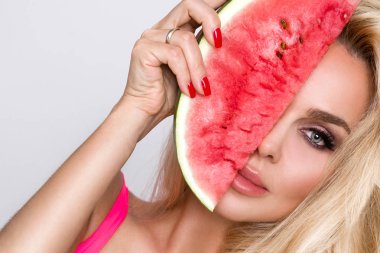 Bir karpuz yüzüne tutarak uzun sarı saçlı güzel kadın modeli