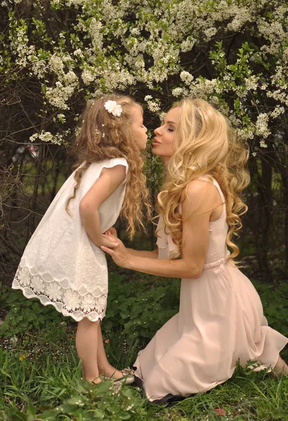 Mooie jonge moeder met haar dochter gekleed in lente kleding zittend op de weide en plezier — Stockfoto