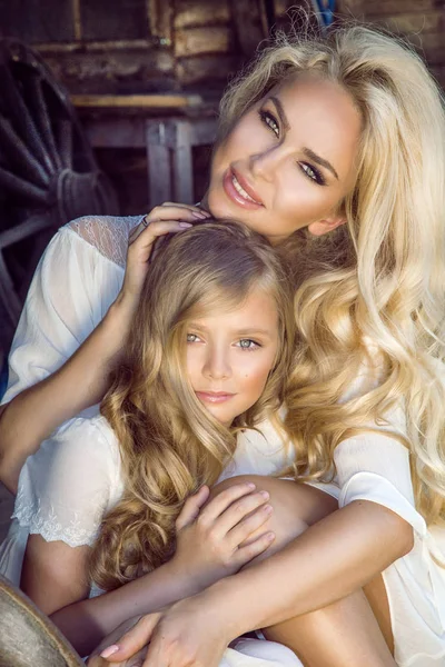 Hermosa madre joven con su hija vestida con ropa de primavera y coronas de flores en la naturaleza — Foto de Stock