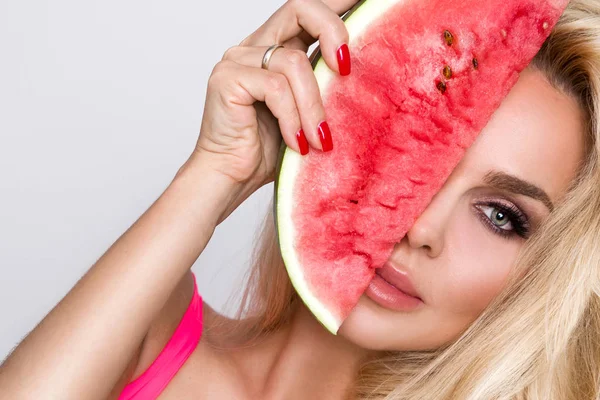 Bir karpuz yüzüne tutarak uzun sarı saçlı güzel kadın modeli