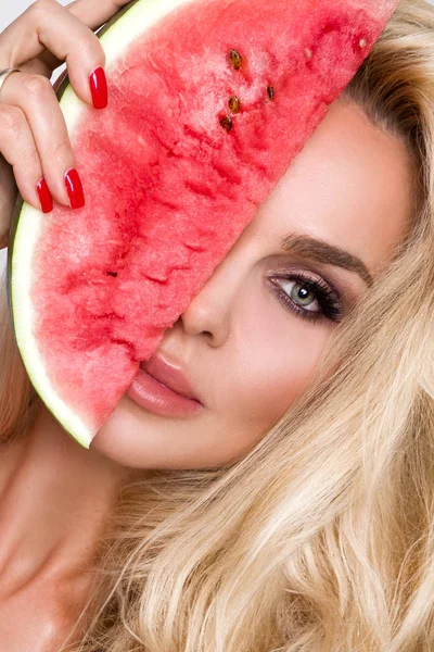 Bir karpuz yüzüne tutarak uzun sarı saçlı güzel kadın modeli