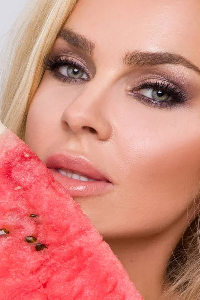 Bir karpuz yüzüne tutarak uzun sarı saçlı güzel kadın modeli