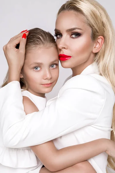 Fantastiska skönhet en ung mor med en söt blond dotter står på en vit bakgrund klädda i en våren kläder — Stockfoto