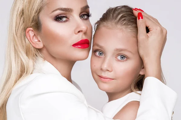 Verbluffende schoonheid een jonge moeder met een schattige blonde dochter staande op een witte achtergrond gekleed in een lente kleding — Stockfoto