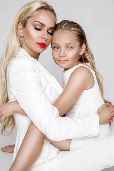 Impresionante belleza una madre joven con una linda hija rubia de pie sobre un fondo blanco vestido con una ropa de primavera —  Fotos de Stock