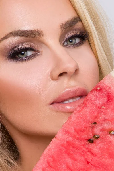 Bir karpuz yüzüne tutarak uzun sarı saçlı güzel kadın modeli