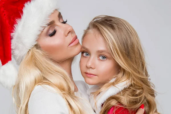 Schöne sexy blonde Mutter mit einem kleinen Mädchen Tochter gekleidet als Weihnachtsmann Umarmung an Weihnachten im Winter und Schnee — Stockfoto