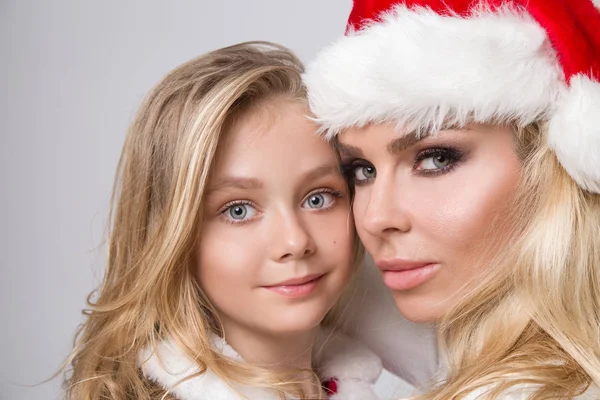 Mooie sexy blonde vrouwelijke model moeder en dochter verkleed als Santa Claus in een rode dop met op de mooie make-up van wit bont in Christmas time — Stockfoto