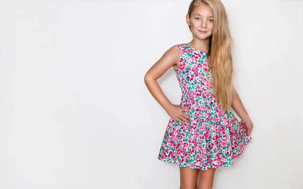 Krásná holčička s dlouhými světlými vlasy a modrýma očima, stojící na bílém pozadí, nosit šaty barevné jarní květy — Stock fotografie