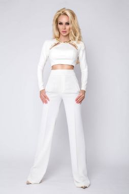 Beyaz bir arka plan beyaz pantolon ve bluz üzerinde duran güzel genç zarif uzun boylu seksi kadın işkadını ve sensually görünüyor
