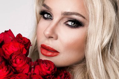 Güzel seksi sarışın beyaz bir arka plan üzerinde zarif iç çamaşırı. Bir buket kırmızı gül tutan kız.