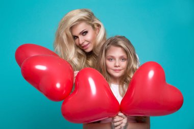 Güzel sarışın anne ve kızı mavi bir arka plan ve holding kırmızı Sevgililer balon üzerinde durmak