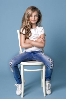 Güzel denim Jeans mavi bir arka plan bir sandalyede oturan küçük sarışın kız çarpıcı