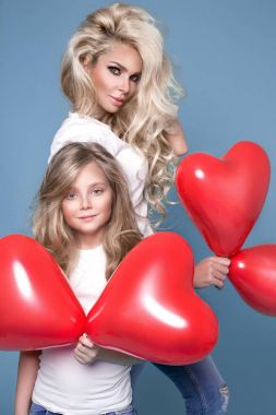 Güzel sarışın anne ve kızı mavi bir arka plan ve holding kırmızı Sevgililer balon üzerinde durmak