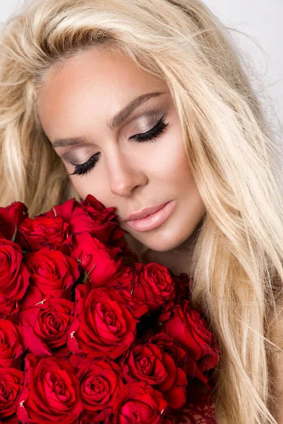 아름 다운 흰색 배경에 우아한 란제리에 섹시 한 금발. 빨간 장미 꽃다발을 들고 소녀. — 스톡 사진