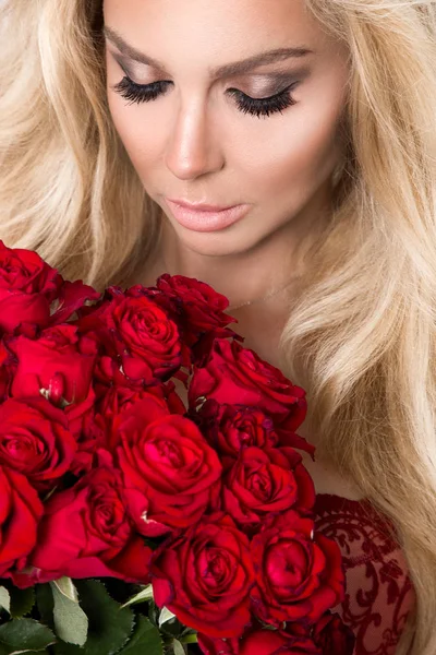 Mooie sexy blonde in elegante lingerie op een witte achtergrond. Meisje met een boeket van rode rozen. — Stockfoto