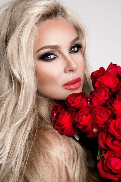 Schöne sexy Blondine in eleganten Dessous auf weißem Hintergrund. Mädchen mit einem Strauß roter Rosen. — Stockfoto